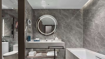 Un baño moderno con pared de mármol, un espejo redondo, una bañera y un mueble de tocador con lavabo y perchero.