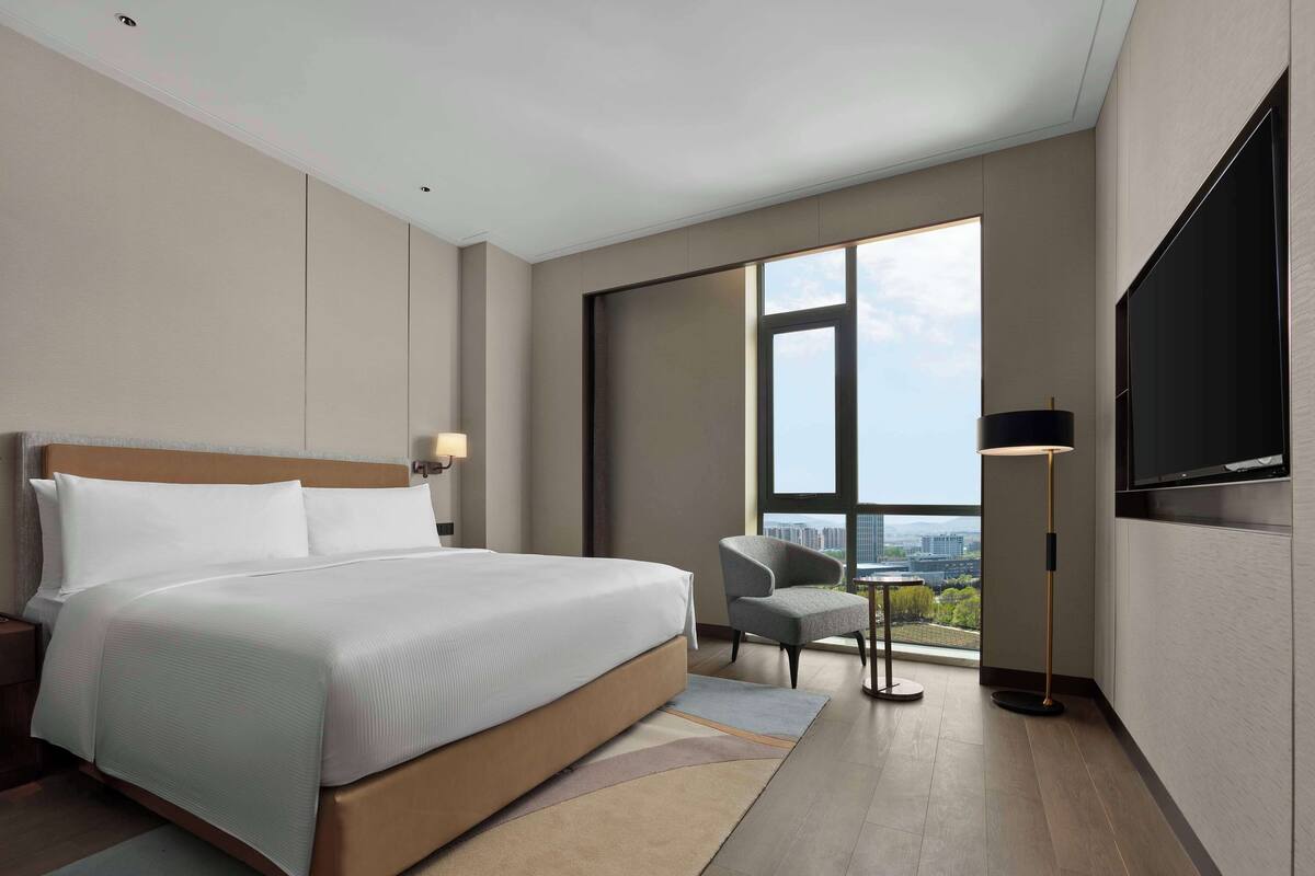 Una habitació d'hotel moderna amb un llit gran, una cadira, una taula petita i una televisió penjada a la paret.