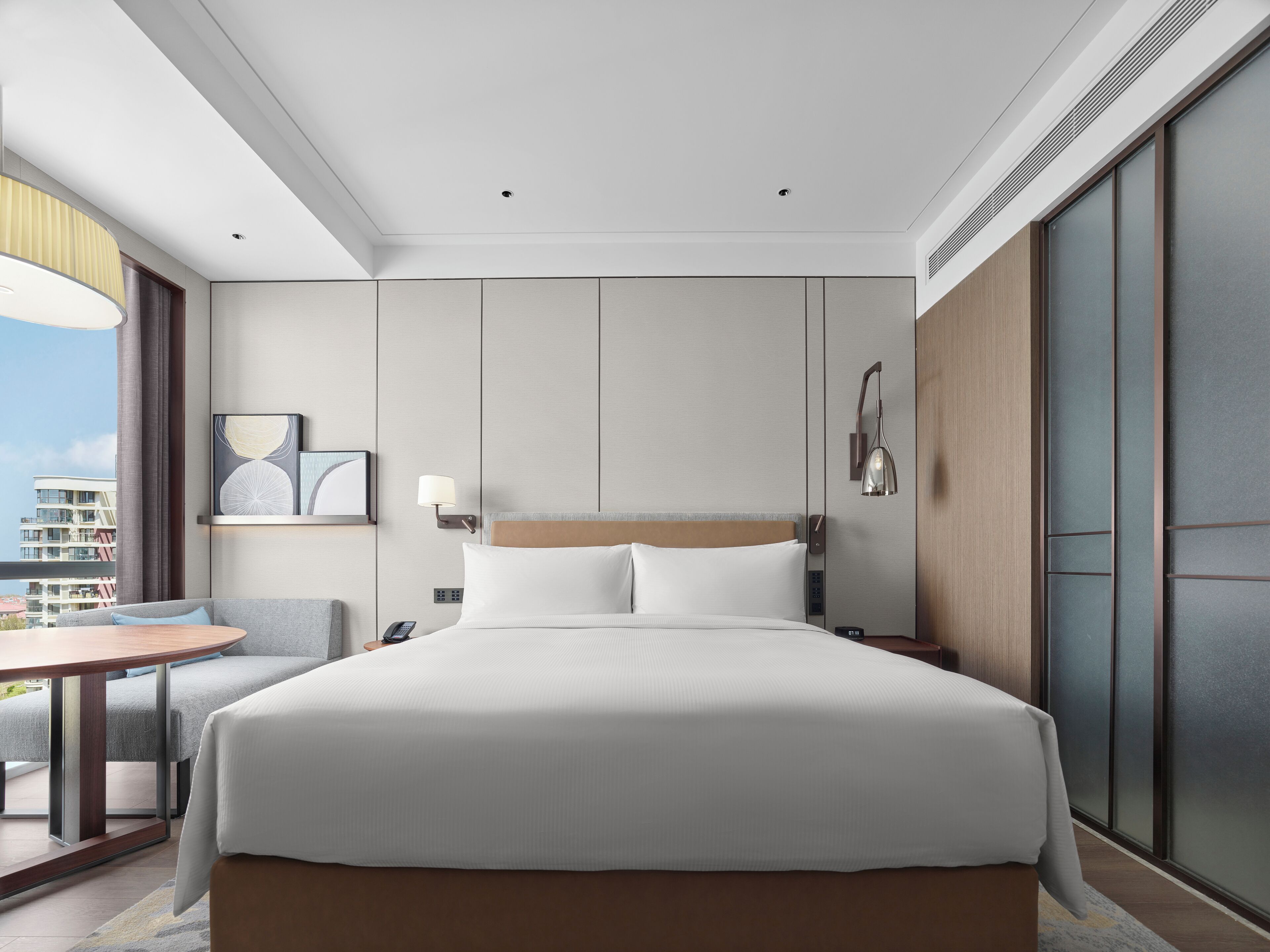 A modern hotel room with a large bed, a bedside table, a desk, and a chair.