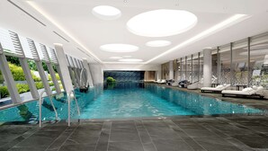 Une piscine intérieure moderne, avec une vue dégagée sur le bassin, des chaises longues et une cascade décorative.