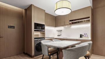 A modern kitchen with wooden cabinetry, a built-in microwave, a coffee machine, and a dining area with a marble table and grey chairs.