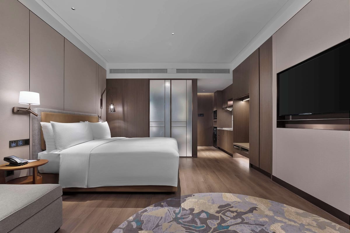 Habitació d'hotel moderna amb un llit gran, una taula de nit, una làmpada i un televisor fixat a la paret.