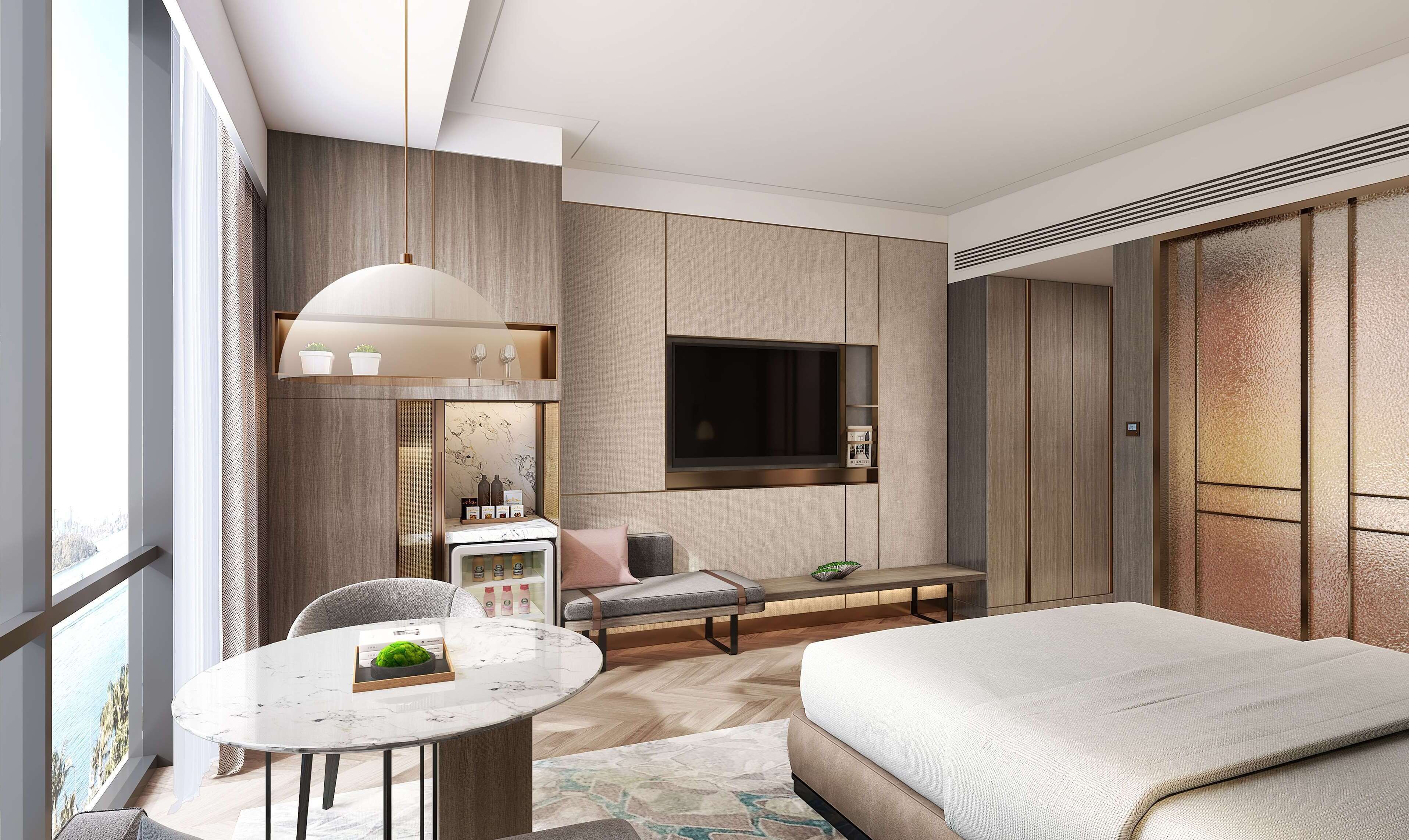 A modern hotel room with a bed, a round dining table, a sofa, a TV mounted on the wall, and a large window offering a view.
