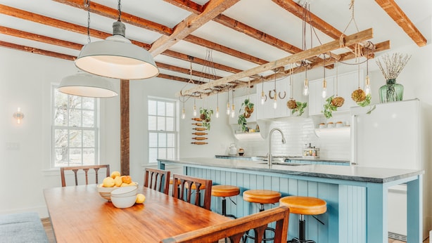A kitchen with wooden beams, a central island with stools, and hanging light fixtures.