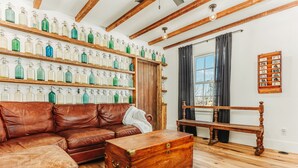 A room with a brown leather sofa, a wooden bench, a wooden chest, and shelves with glass bottles.