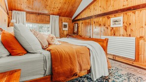 A wooden cabin bedroom with a bed, a nightstand, a window with curtains, and a radiator.