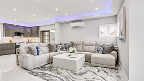 Una sala de estar moderna con un sofá seccional, una mesa de centro y una cocina al fondo.
