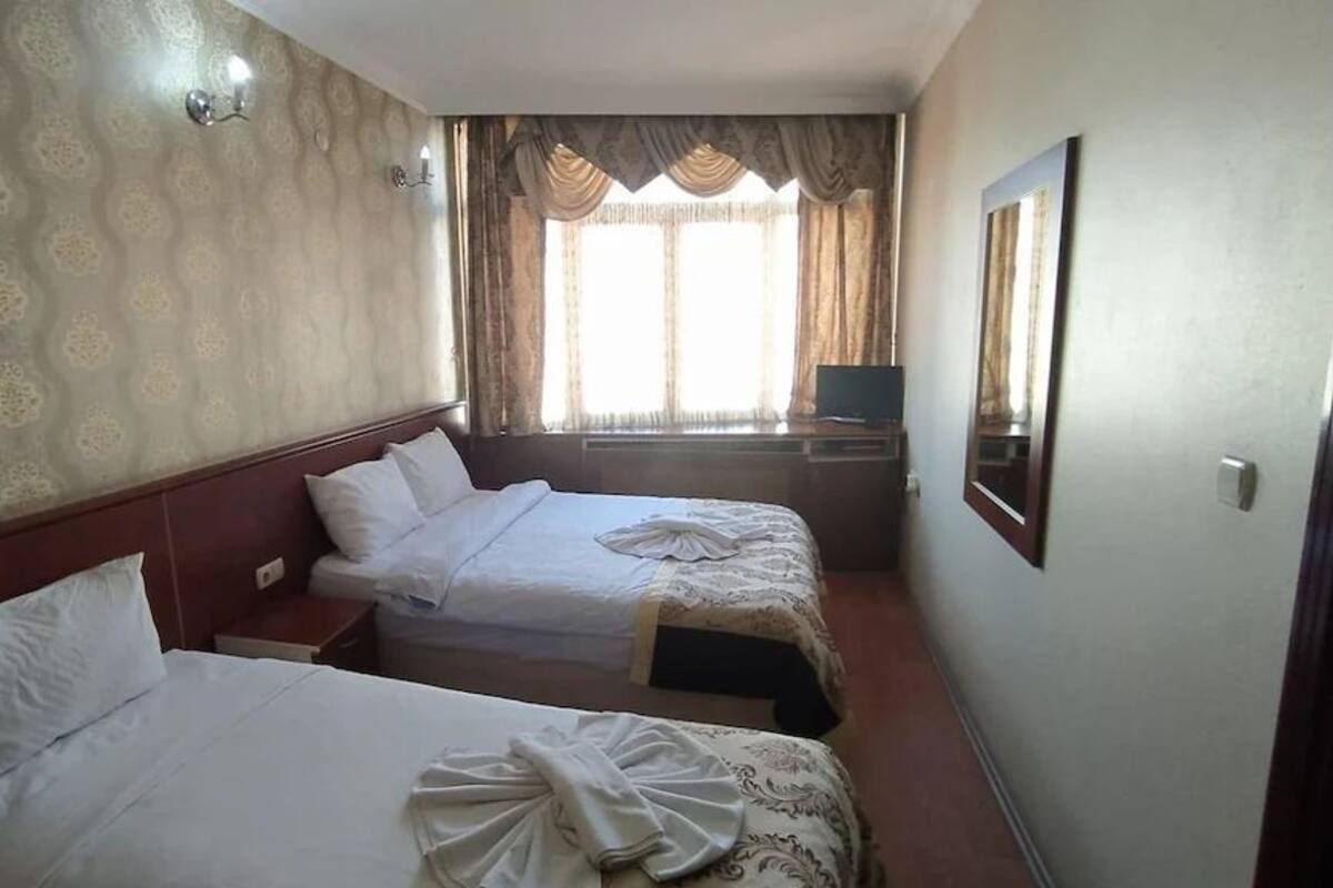 A hotel room with two beds, a large mirror, and a window with curtains.