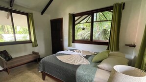 Een slaapkamer met een bed, een bankje, een raam met gordijnen en een lamp.