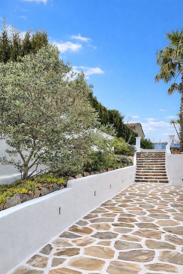 A stone pathway leading to a white-walled building with a staircase.