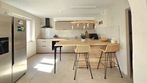 A modern kitchen with a stainless steel refrigerator, a central island with bar stools, a black range hood, and a white tiled backsplash.