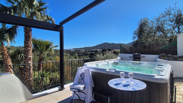 A hot tub on a balcony with a view of palm trees and a mountain.