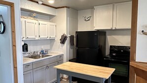 A compact kitchen with white cabinets, a black refrigerator, and a wooden table. - Waterfront 2 Bedroom/Duplex H/Remodeled 2024 (Grove)