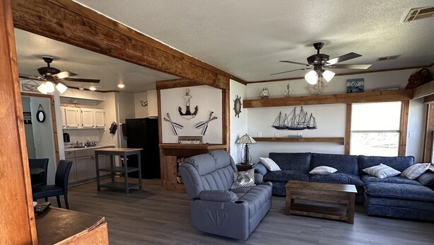 A spacious living area with a sofa, a coffee table, and a dining table. There are ceiling fans and a kitchen in the background. - Waterfront 2 Bedroom/Duplex H/Remodeled 2024 (Grove)