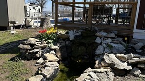 A covered outdoor area with a stone pond, wooden deck, and a view of a residential neighborhood. - Waterfront 2 Bedroom/Duplex H/Remodeled 2024 (Grove)