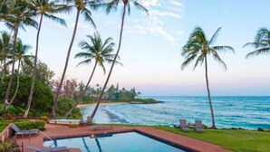 A pool with lounge chairs, palm trees, and a view of the ocean. - Luxury Gated Oceanfront Condo on Ground Floor (Kauai County)