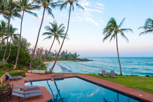A pool with lounge chairs, palm trees, and a view of the ocean.