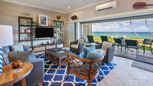 A spacious living room with a large TV, comfortable seating, and a view of the ocean. - Luxury Gated Oceanfront Condo on Ground Floor (Kauai County)