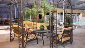 A covered outdoor seating area with wicker furniture and a pool in the background.