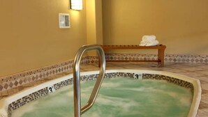 A hot tub with a metal ladder, a bench with towels, and a tiled floor.