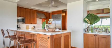Una cocina moderna con armarios de madera, una isla central con taburetes de bar, electrodomésticos de acero inoxidable y un amplio ventanal con vistas.