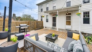 Ein Garten mit Holzterrasse, Gartenmöbeln, Grill und hängenden Blumenkörben.