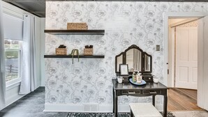 Ein Flur mit blumigem Wandpapier, einem dunklen Holzkonsole und einem Spiegel, Regalen mit Körben sowie einer Bank.