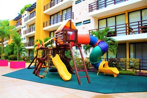 An outdoor play area with slides and climbing structures, surrounded by a building with balconies and windows.