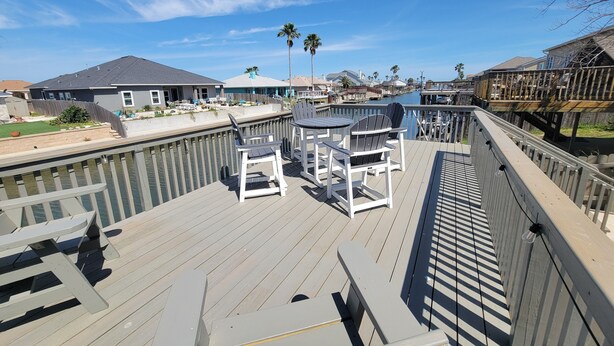 Een houten terras met tuinmeubilair, met uitzicht op een jachthaven met boten en huizen op de achtergrond.