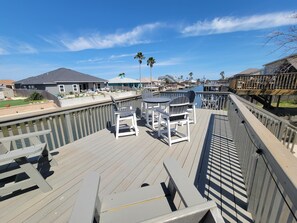 Une terrasse en bois, agréée de mobilier d’extérieur, qui offre une vue sur une marina, avec des bateaux et des maisons en arrière-plan.