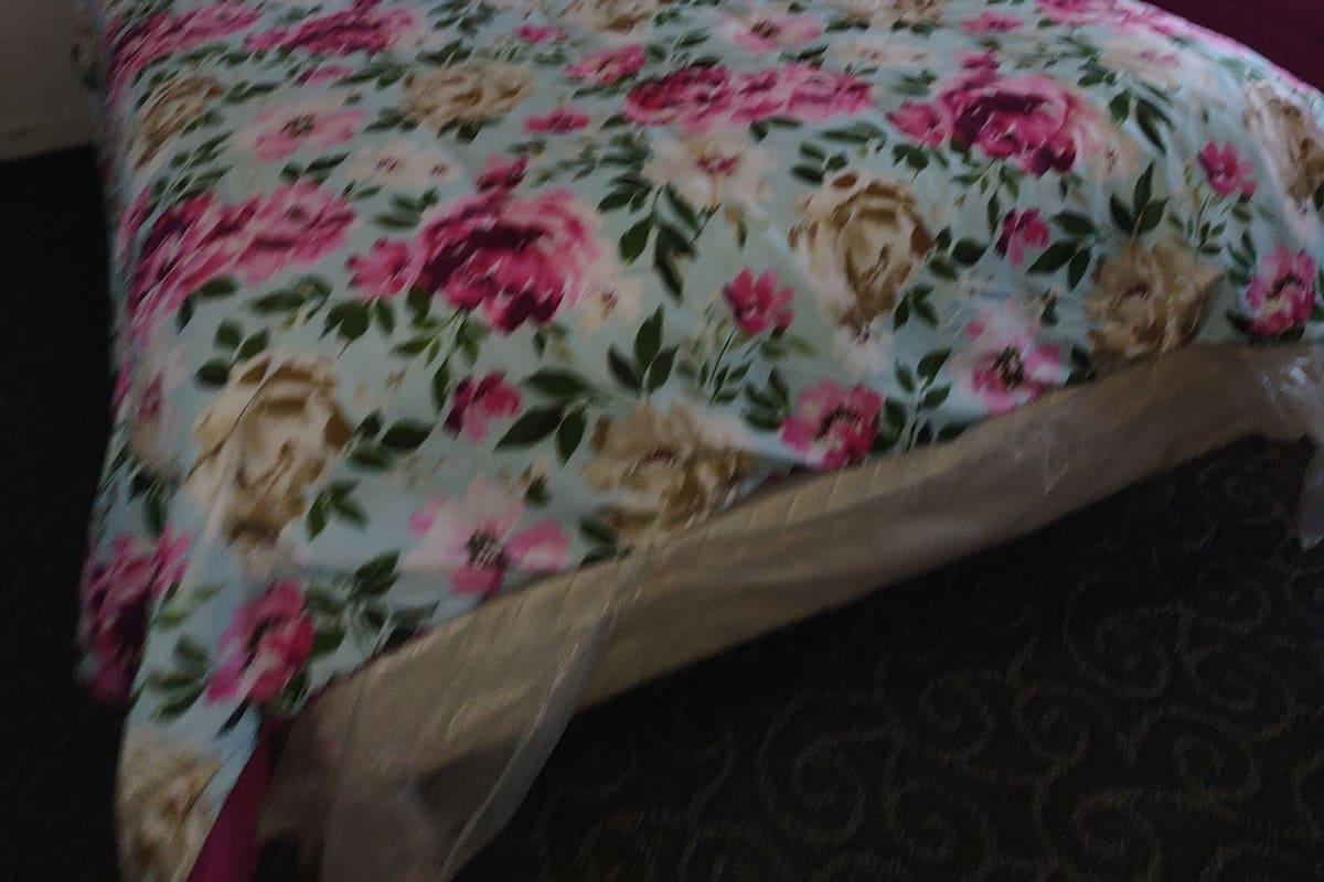 A bed with a floral bedspread, a pink pillow, and a framed picture on the wall.