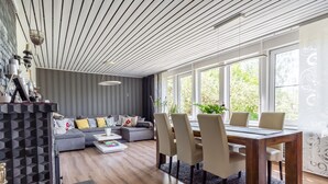 Una sala de estar moderna con un sofá gris, una mesa de comedor con sillas y un techo de madera.