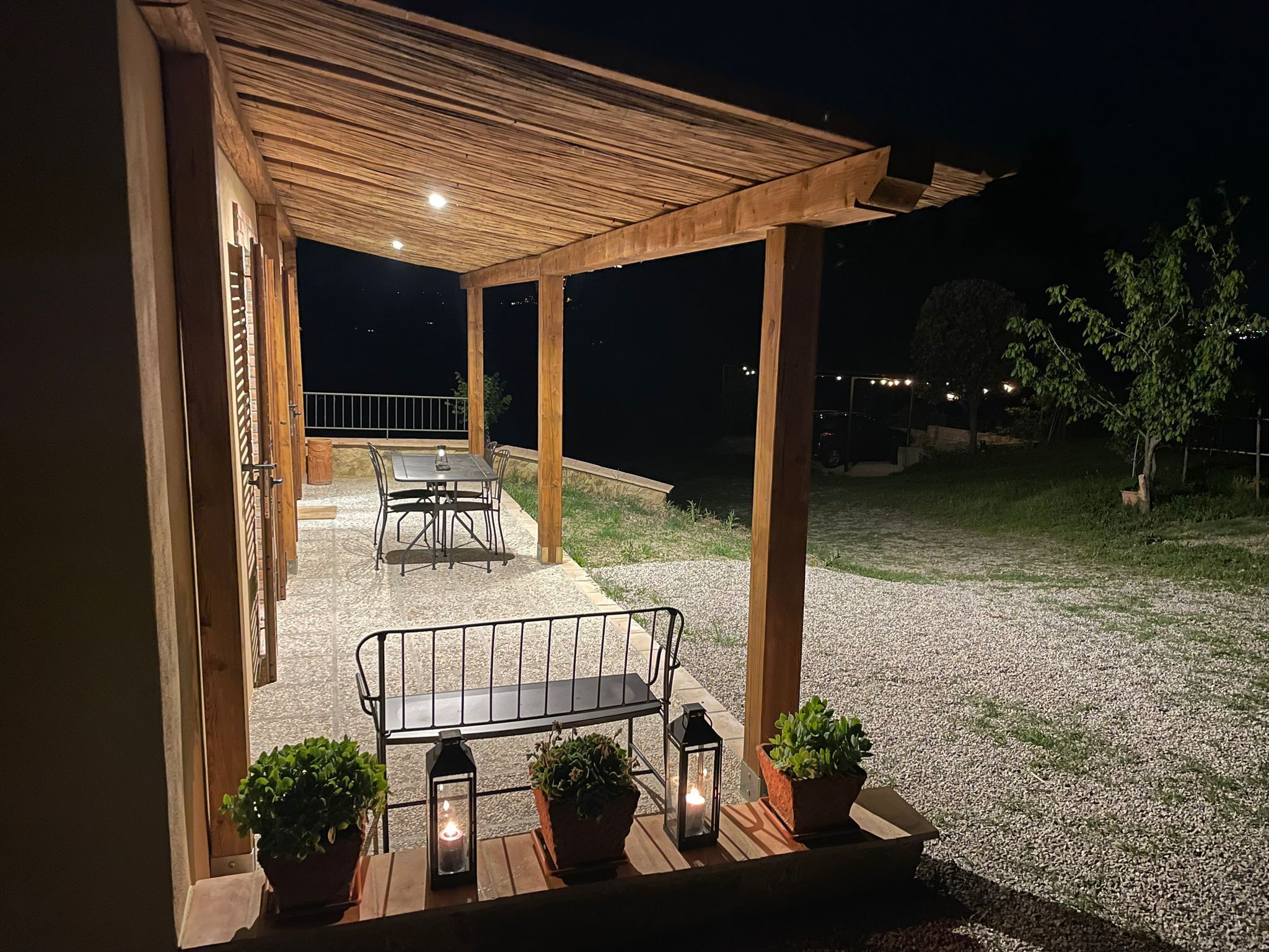 An outdoor patio area with a wooden pergola, a table with chairs, and potted plants.