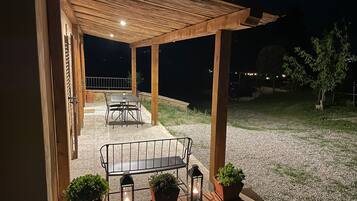 An outdoor patio area with a wooden pergola, a table with chairs, and potted plants.