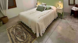 A bedroom with a large bed, a nightstand, a bedside table, a mirror, a window with blinds, and a patterned rug. - Suite Gioconda - Podere Casa Rossa in Pienza (Pienza)