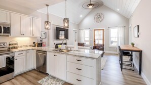 A spacious kitchen with white cabinetry, a large island, and a dining area with a wooden table and chairs. - River View Getaway by 2DC (Gilmer County)