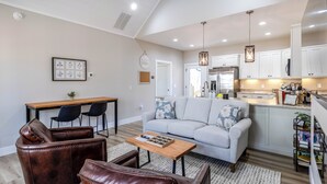 A modern living room with a sofa, leather chairs, a coffee table, and a dining area with a wooden table and chairs. - River View Getaway by 2DC (Gilmer County)