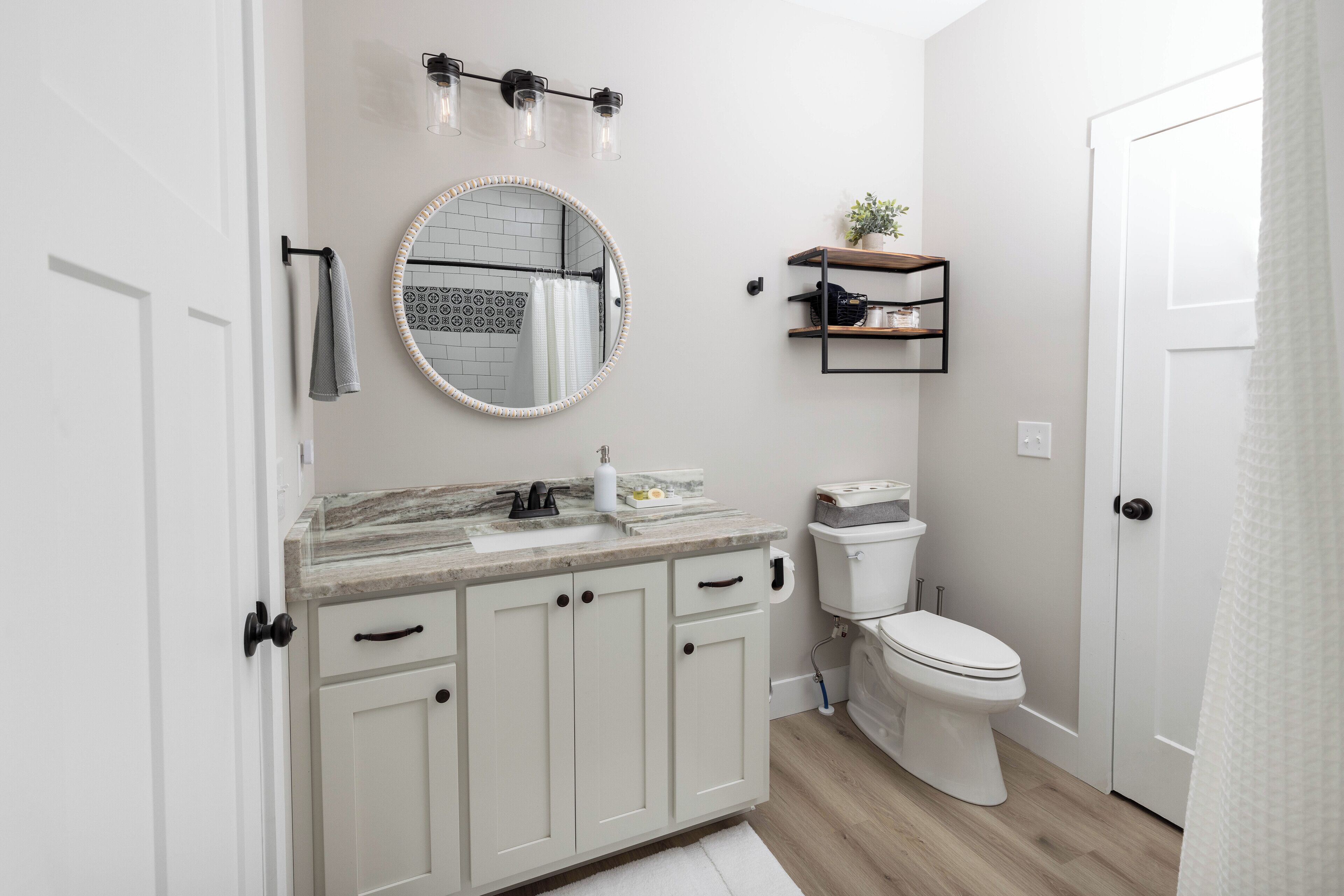 Een moderne badkamer met een wit toilet, een ronde spiegel, een marmeren aanrechtblad en een klein plankje met een plant.