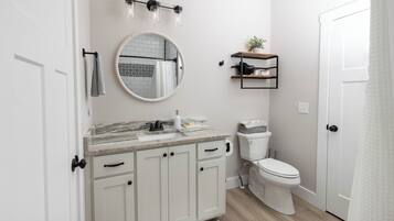 Een moderne badkamer met een wit toilet, een ronde spiegel, een marmeren aanrechtblad en een klein plankje met een plant.