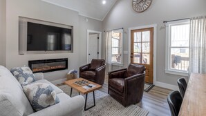 A living room with a fireplace, leather chairs, a sofa, a coffee table, and a TV. - River View Getaway by 2DC (Gilmer County)