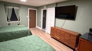 Una habitación con dos camas, televisor, cómoda y una puerta que da a un armario.