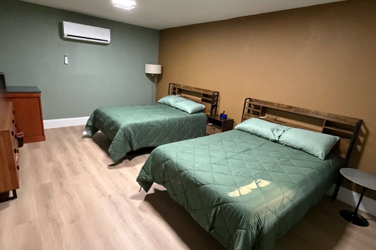 A room with two beds, a desk, a lamp, and an air conditioner.