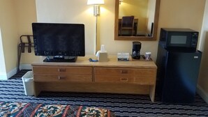 Habitación de hotel con un escritorio de madera, un televisor de pantalla plana, una lámpara, una cafetera, un microondas y un cesto de basura.