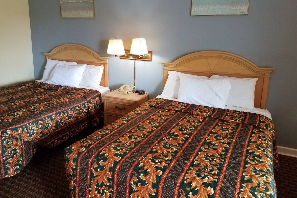 A hotel room with two beds, each with a patterned bedspread, a nightstand with a lamp, and a phone.