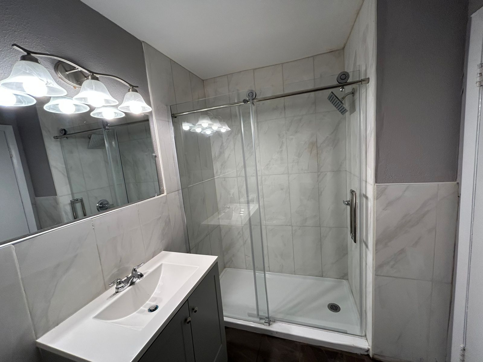 Un baño moderno con ducha separada por mampara de vidrio, un lavabo blanco y un espejo grande.