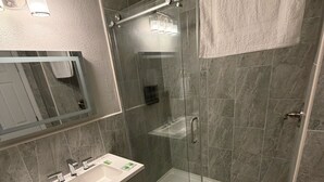 Un baño moderno con ducha envuelta en vidrio, tocador con lavabo y espejo.