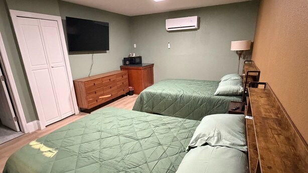 Un dormitorio con dos camas, un aparador, un televisor y aire acondicionado.