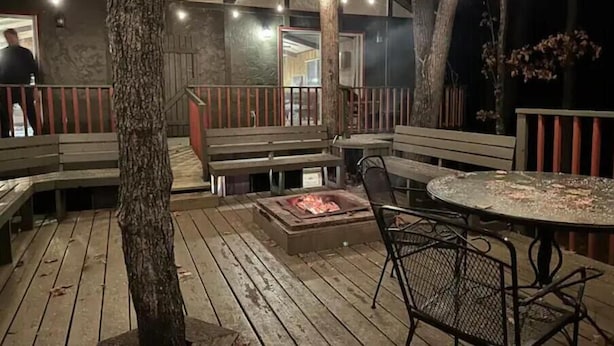 En udendørs terrasse med træbænke, et bålsted og et bord.