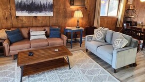 En hyggelig stue med en trævæg, et stort maleri, en sofa, et sofabord og en lampe.