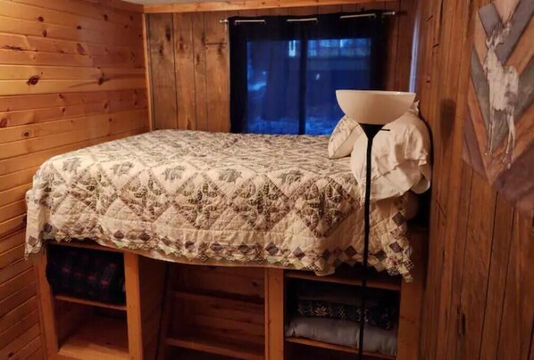 A cozy cabin room with a bed, a lamp, and wooden walls.